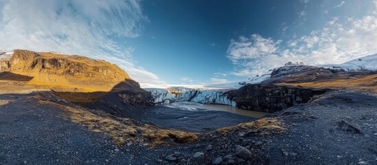 Naklejka premium Glacier tongue in a valley, surrounded by dark mountains under a partly cloudy blue sky.