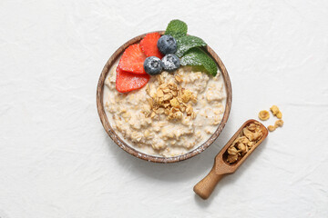 Bowl with tasty oatmeal, mint leaves and berries on white grunge background