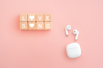 LOVE SONG text on wooden cube blocks with bluetooth white earphone with case on pink background
