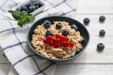 Bowl with tasty oatmeal and berries on white wooden background, closeup