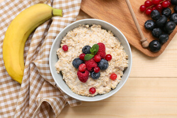 Bowl with tasty oatmeal and berries on wooden background