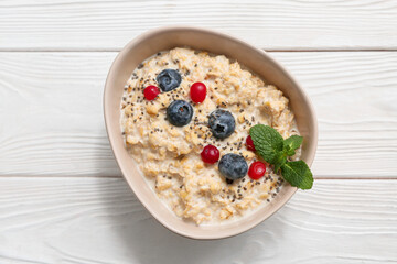 Bowl with tasty oatmeal, berries and chia seeds on white wooden background