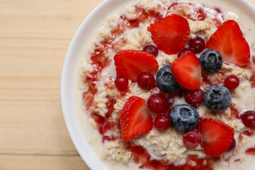 Bowl with tasty oatmeal, syrup and berries on wooden background, closeup
