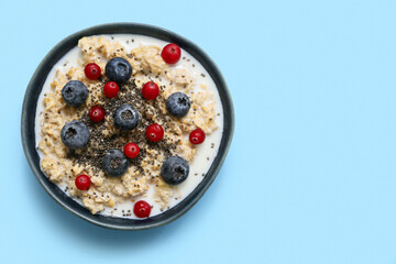 Bowl with tasty oatmeal, chia seeds and berries on blue background