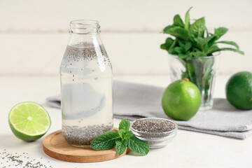 Bottle of water with chia seeds, limes and mint on white table against wooden background