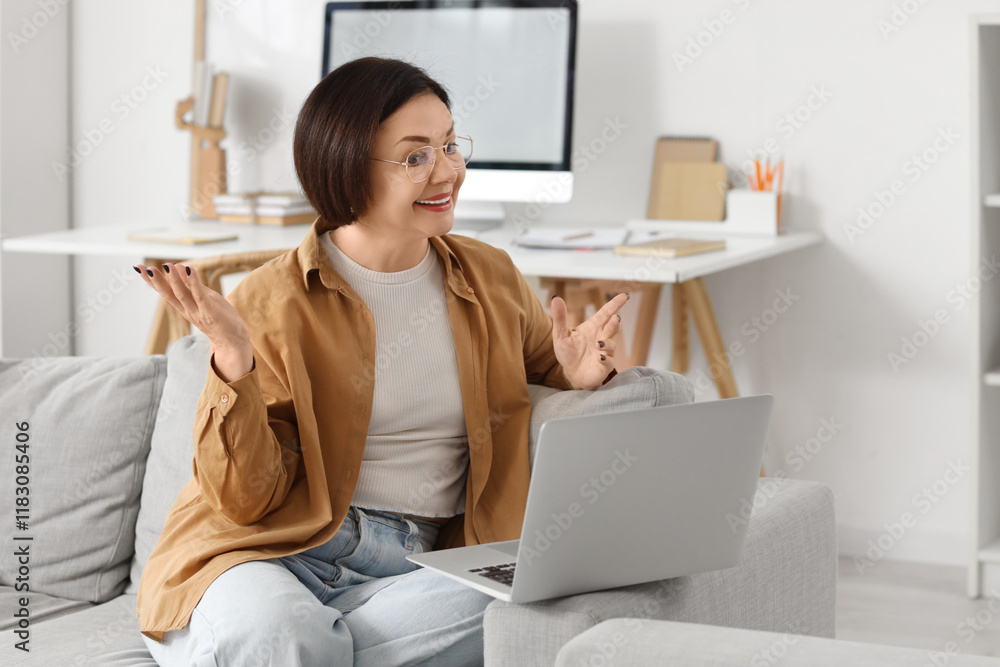 Poster Mature woman with laptop video chatting on sofa at home