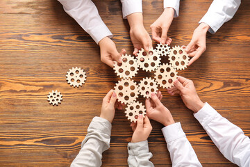 Hands holding wooden gears on wooden background, top view
