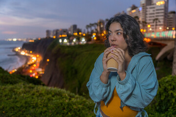 Young woman enjoying a coffee break at sunset overlooking the city lights of lima, peru