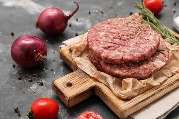 Cutting board with raw meat cutlets on grey grunge background, closeup