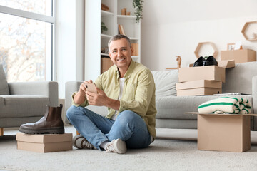 Mature man using mobile phone with boxes of clothes at home