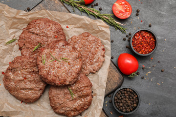 Wooden board with tasty meat cutlets, tomatoes, spices and rosemary on black grunge background
