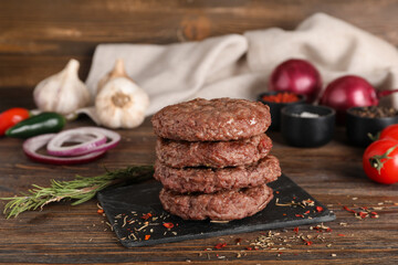 Board with stack of tasty meat cutlets, rosemary and spices on wooden background