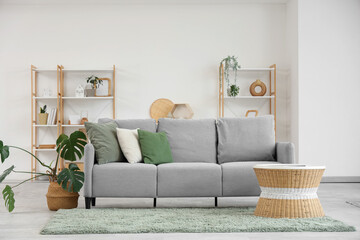 Interior of light living room with grey sofa, coffee table and shelf units