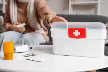 Woman with first aid kit and cold medicines on table at home, closeup