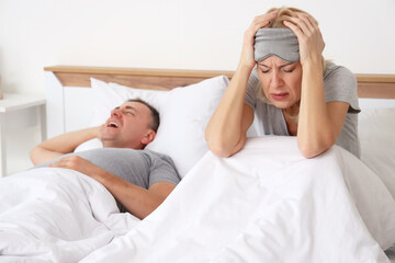 Irritated mature woman with her snoring husband in bedroom