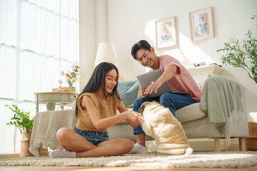 Young Asian Couple Enjoying at Home While Playing With a Pet dog and Using a Laptop Together.