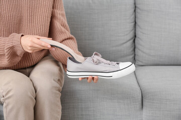 Young woman putting orthopedic insole into sneaker on sofa at home, closeup