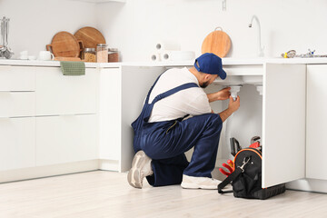 Male plumber repairing sink pipe in kitchen © Pixel-Shot