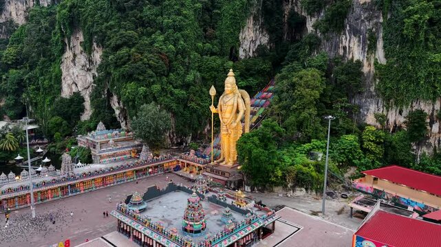 Drone video Batu Caves Hindu temple in Kuala Lumpur, Malaysia. Aerial footage shows tall golden Murugan statue and stairs leading up to caves.