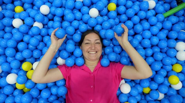 Woman lying down, playing and throwing balls in a ball pit