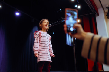 Mother Filming her Daughter Singing and Performing on a Stage . Girl reciting a poem on in a public...