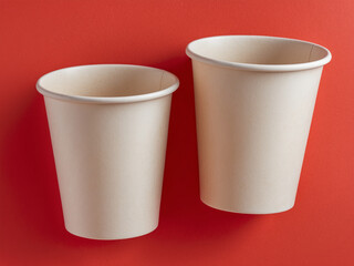 Two light beige disposable paper cups placed side by side against a vibrant red background. Ideal for eco-friendly, takeaway, and beverage-related themes.