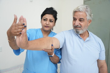 Indian female physiotherapist help mature man with stretching arms exercise to recover from injury at health center. caregiver in nursing care support senior patients at rehabilitation. Rehab fitness,