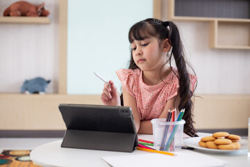 Little girl doing homework with modern tablet at home