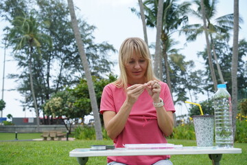 Young woman beading colorful bracelets outdoors in a park