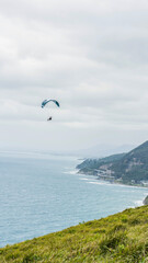 A lone paraglider in the distance hangs above the coastline on the south coast of New South Wales.