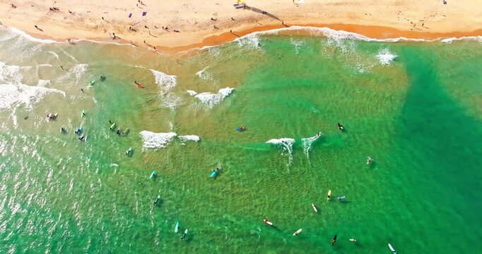 aerial top view of beautiful sunny beach with waves hitting the coast, tourist walking on the golden sand,people surfing in the wave at Wanning China