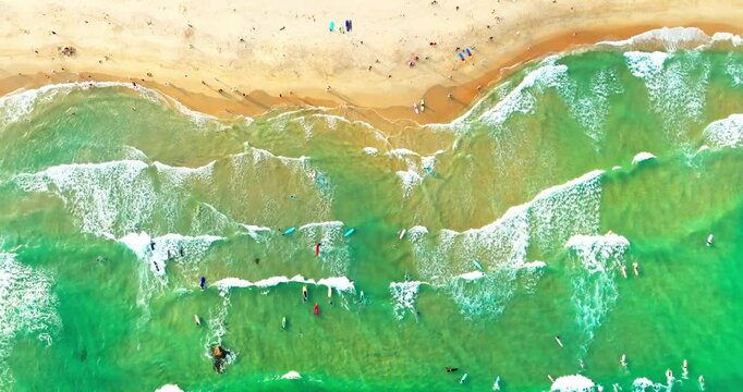 aerial top view of beautiful sunny beach with waves hitting the coast, tourist walking on the golden sand,people surfing in the wave at Wanning China