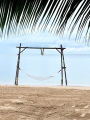 Wooden swing on the beach with the foreground of palm tree