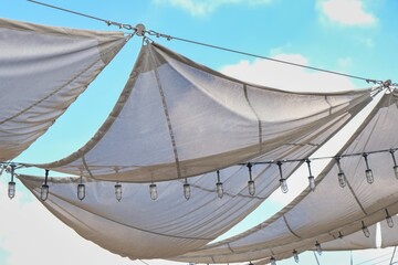 Outdoor airy canopy construction of fabric stretch roof made of canvas sail with rows of bulb lamps...
