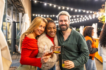 Friends smiling toasting at camera in a bar at night