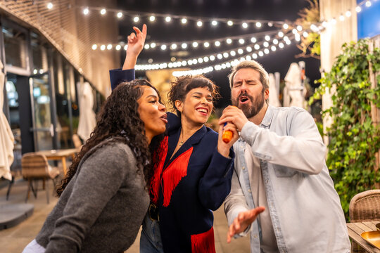 Happy friends singing karaoke passionately during night party outdoors