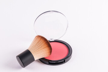 An open round pack of compact blush in a pink tone with a professional fluffy short makeup brush....
