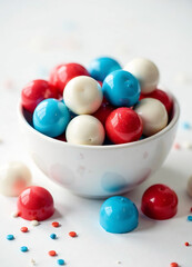 A white bowl filled with colorful candy-coated chocolates in red, white, and blue, with some scattered around the bowl on a white background. new image