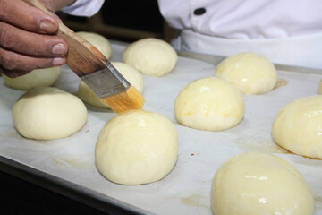 Brushes the tops of round bread rolls with a golden liquid with egg wash before baking them