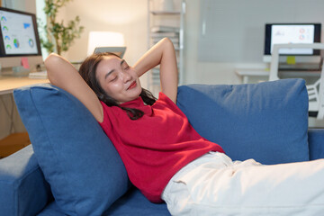 Young asian businesswoman relaxing on the sofa with hands behind her head, eyes closed, enjoying a moment of peace and quiet after a productive day working from home