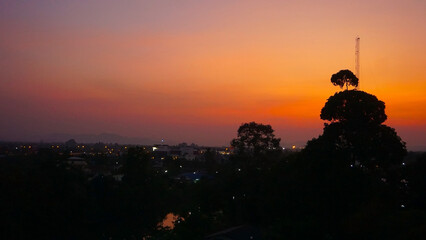 Obraz premium Sunset Cityscape Silhouette. A breathtaking view of a city silhouetted against the fiery hues of a setting sun. The warm glow of the sky casts a magical ambiance over the cityscape.