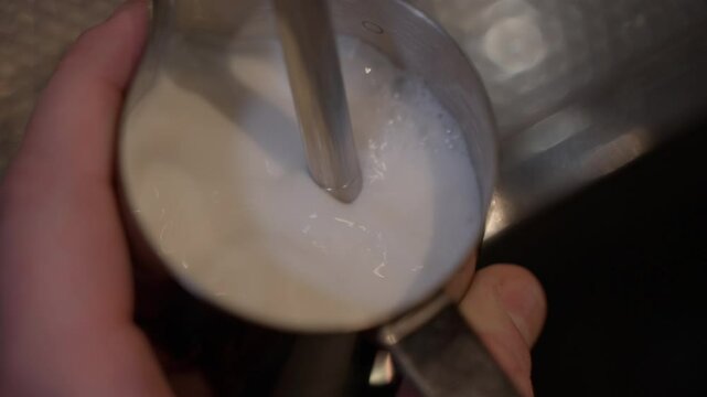 Tiny bubbles emerge on milk surface turning into creamy foam. Satisfying moment of barista magic where every bubble tells story of barista precision