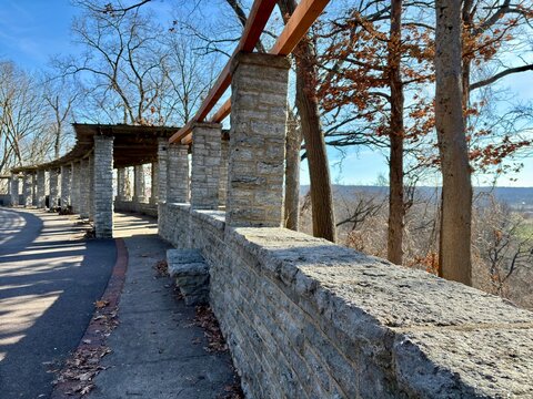 Stone pergola with wooden beams, curved pathway, scenic woodland view