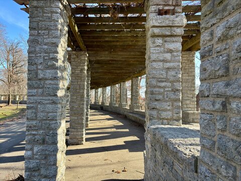 Stone pergola with wooden beams and textured columns casting shadows