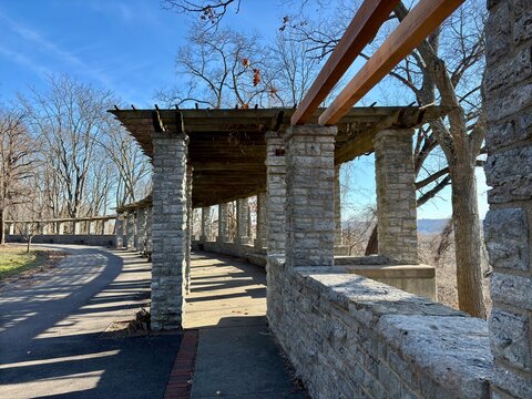 Stone pergola with wooden beams, curved pathway under clear blue sky