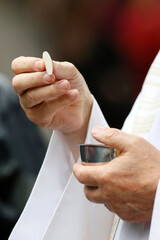 Catholic Mass. Priest giving Communion. Host symbolizing the body of Christ. Close up on hand.