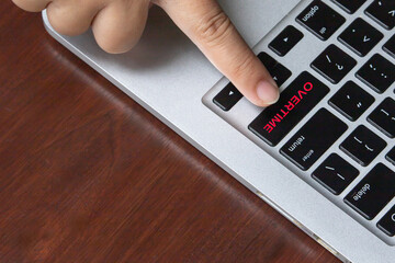 Close-up of a hand pressing a keyboard key labeled "Overtime," symbolizing extended working hours, job stress, and workplace dedication.