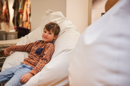 Boy lounging on a white beanbag chair in a cozy store setting.