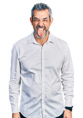 Fototapeta premium Middle age hispanic with grey hair wearing casual white shirt sticking tongue out happy with funny expression. emotion concept.