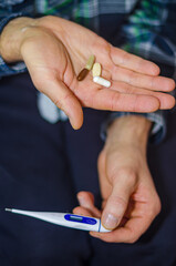 Close-up of a person's hands holding a digital thermometer and various pills. High quality photo